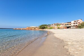 A beach with clear water, sandy shore, and buildings in the background.