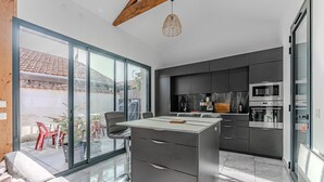 A modern kitchen with a large island, built-in appliances, and a sliding glass door leading to an outdoor patio.