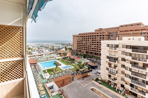 A high-rise hotel with a pool area, multiple balconies, and a view of the sea.