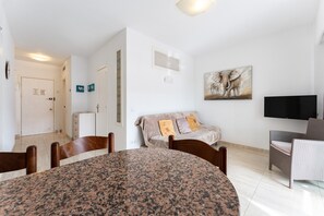 A room with a dining table, chairs, a sofa, a television, and a painting on the wall.