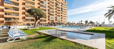 A hotel with a swimming pool, a grassy area, and a large building with multiple balconies.