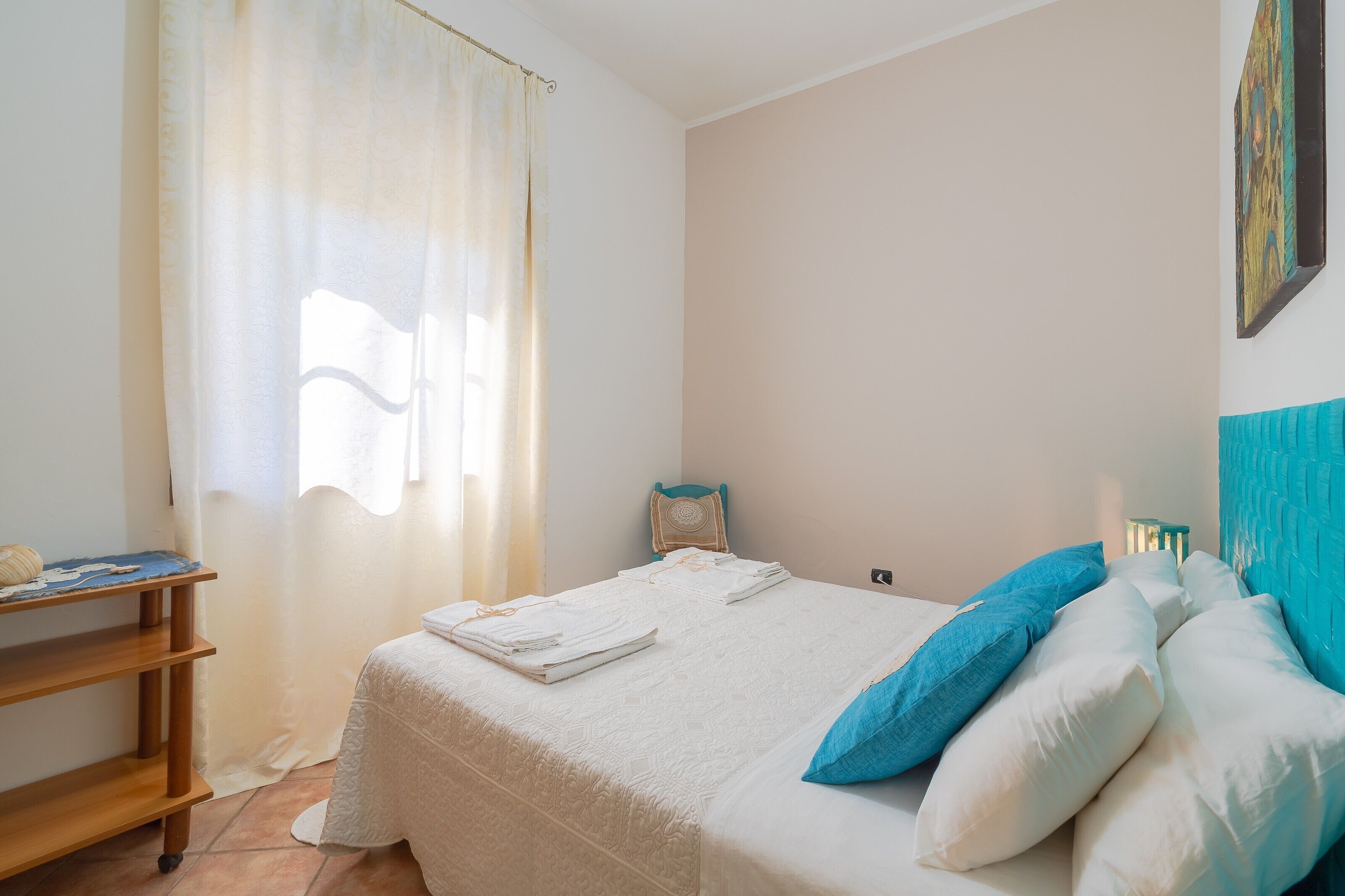 Quarto com cama, travesseiros, prateleira e janela com cortinas.