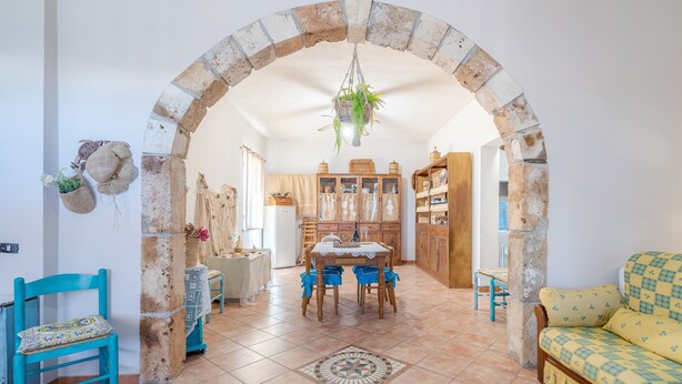 A spacious living area with a stone archway, a dining table with chairs, a sofa, and a kitchen in the background. - Apartment "Sara Home" with Sea View, Private Terrace & Wi-Fi (Portopalo di Capo Passero)