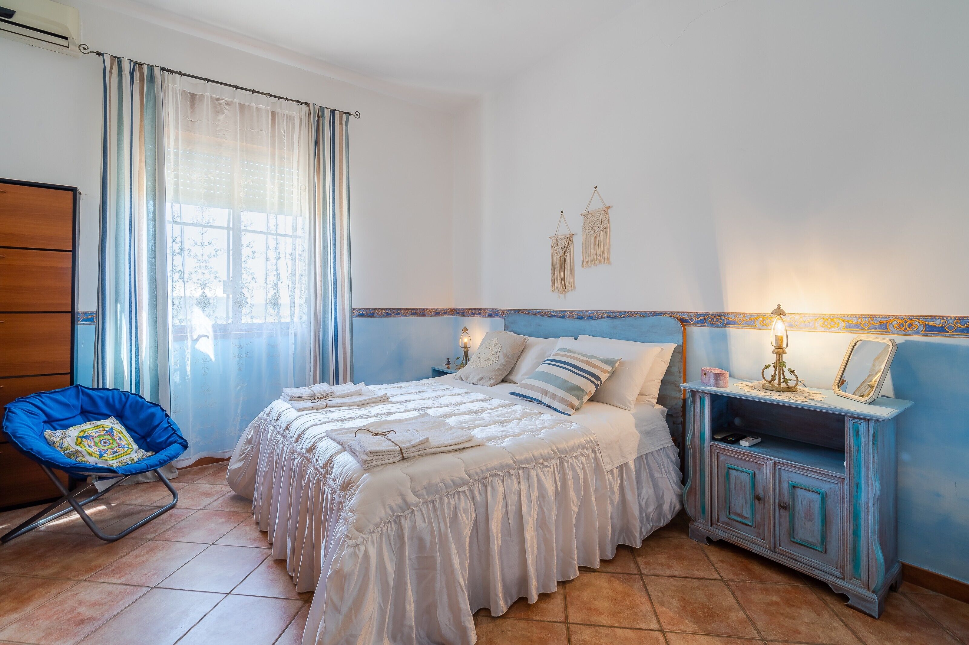 A bedroom with a bed, a chair, a nightstand, and a dresser.