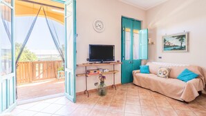 A room with a TV on a stand, a sofa with cushions, a clock on the wall, and a door leading to an outdoor area. - Apartment "Sara Home" with Sea View, Private Terrace & Wi-Fi (Portopalo di Capo Passero)