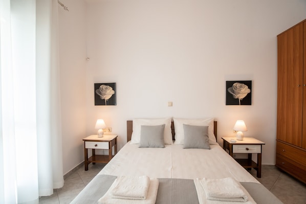 A bedroom with a large bed, two bedside tables with lamps, a wooden wardrobe, and two wall-mounted flower paintings.