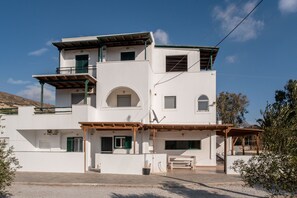 A multi-story building with a flat roof, a balcony on the upper floor, and a covered outdoor seating area.
