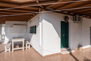 A covered outdoor area with a wooden table and benches, a green door, and an air conditioning unit.