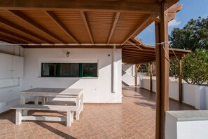 An outdoor patio with a wooden pergola, a white table, and a window.