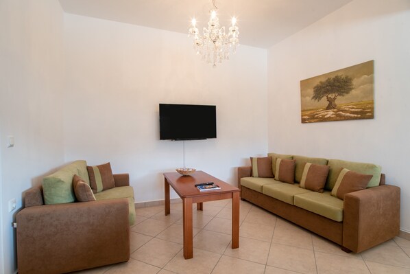 A living room with two sofas, a coffee table, a TV mounted on the wall, and a chandelier.