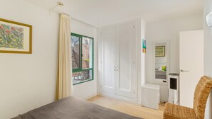 Ett sovrum med en säng, en stol, en garderob, ett litet skrivbord och ett fönster med gardiner.