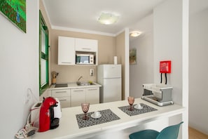 A compact kitchen with white cabinets, a microwave, a refrigerator, a coffee machine, and two glasses on a placemat. - Vacation Home 'Casa Orballo' with Shared Pool, Private Terrace and Wi-Fi (Mogán)