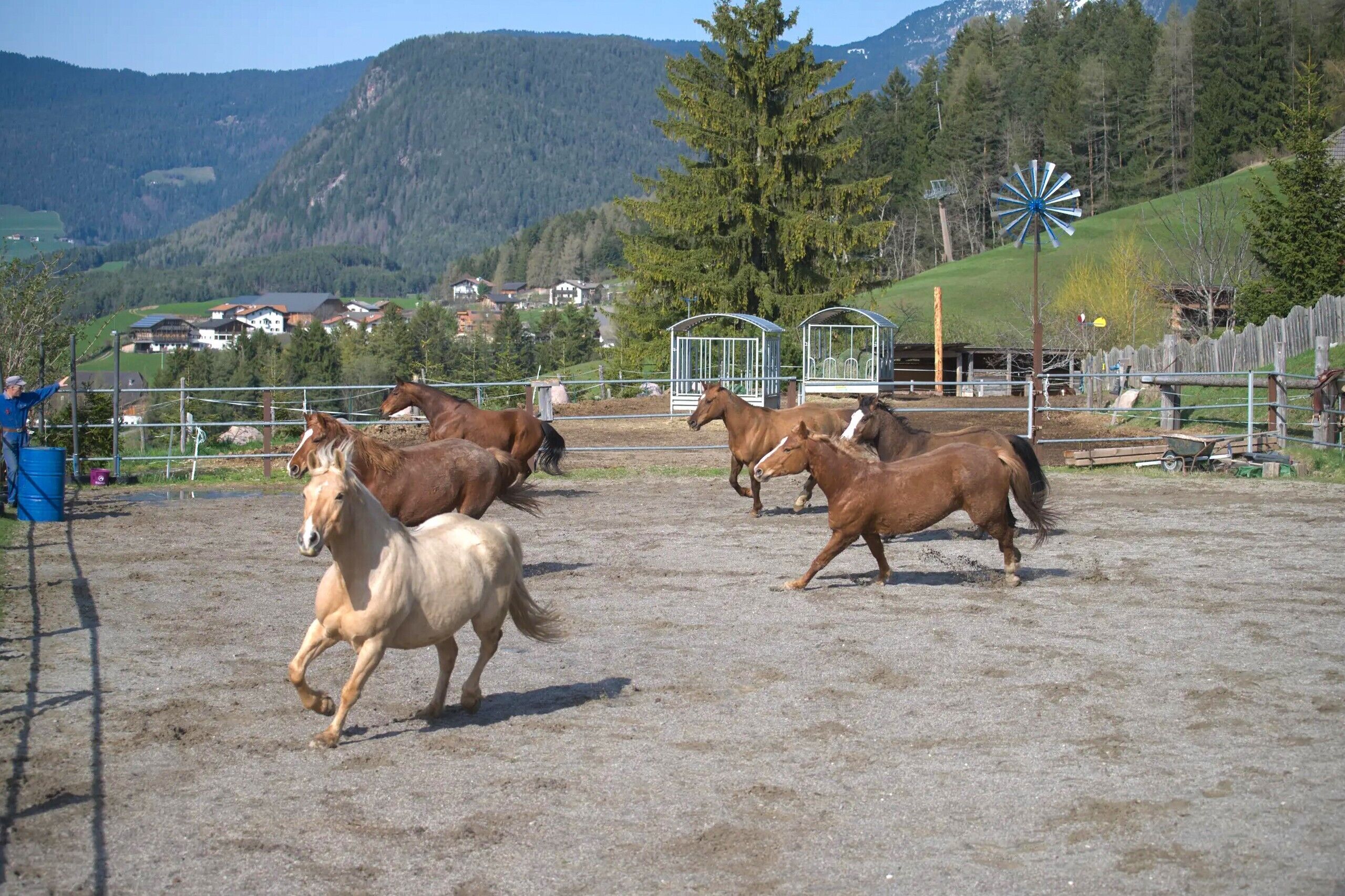 A stable with horses, a windmill, and a mountainous backdrop.