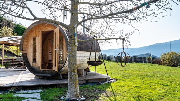 Una estructura de madera con un orificio circular, un árbol y un objeto metálico colgando.