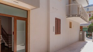 Um edifício com entrada por porta de vidro, escada e pequena varanda com grade de metal.