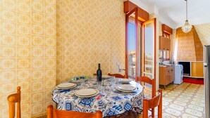 Uma sala de jantar com uma mesa redonda posta para quatro pessoas, uma cozinha ao fundo e papel de parede estampado.