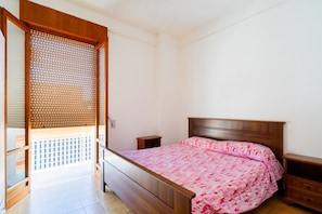 A bedroom with a wooden bed, a nightstand, a wooden wardrobe, and a sliding door leading to a balcony.