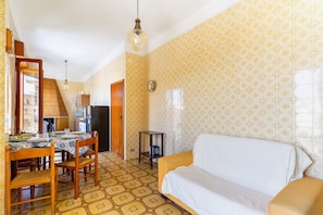 A dining area with a table set for four, a sofa, a small side table, and a patterned wall.