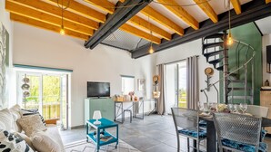 A spacious living area with a sofa, dining table, chairs, a TV, and a staircase. - "Le Kerhuel d'Agnès" with private terrace, private garden and Wi-Fi (Plouasne)