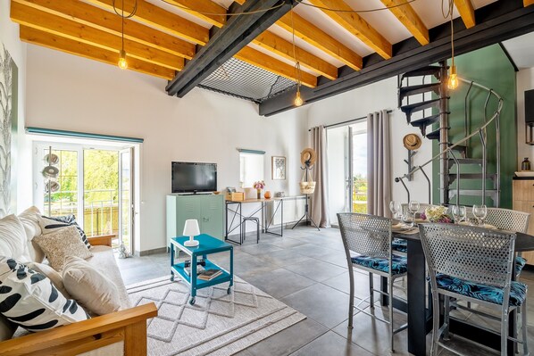 A spacious living area with a sofa, dining table, chairs, a TV, and a staircase.