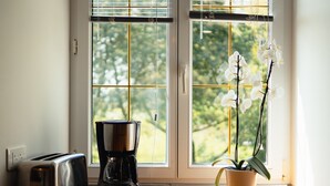 A kitchen with a toaster, coffee maker, and a potted orchid by a window. - "Le Kerhuel d'Agnès" with private terrace, private garden and Wi-Fi (Plouasne)