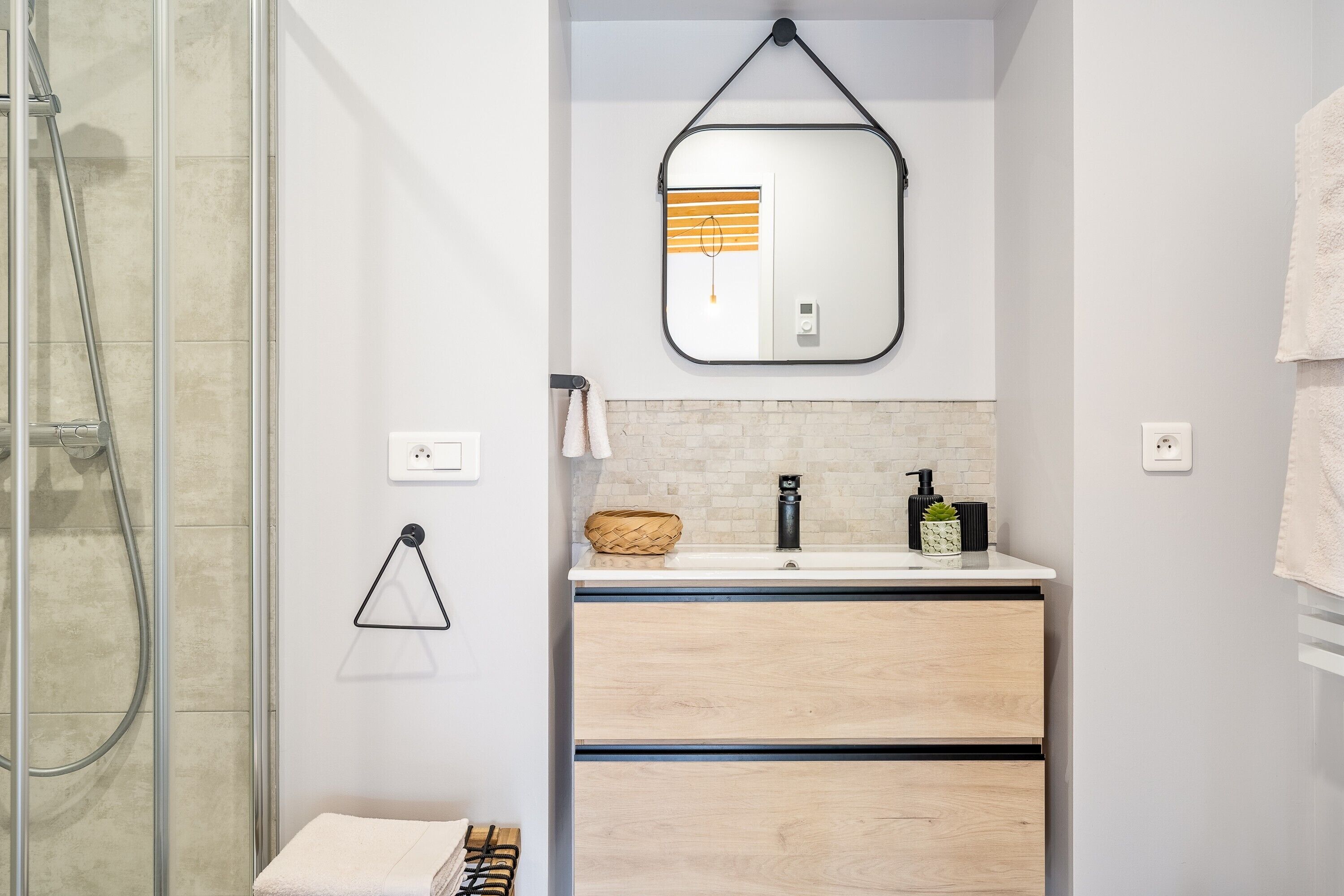 Ein modernes Badezimmer mit Duschkabine aus Glas, einem Holzkosmetikschrank mit Spiegel und einem Handtuchhalter.