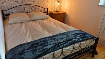 Een bed met hoofdeinde, een nachtkastje met lamp, en een muur met bloemenbehang.