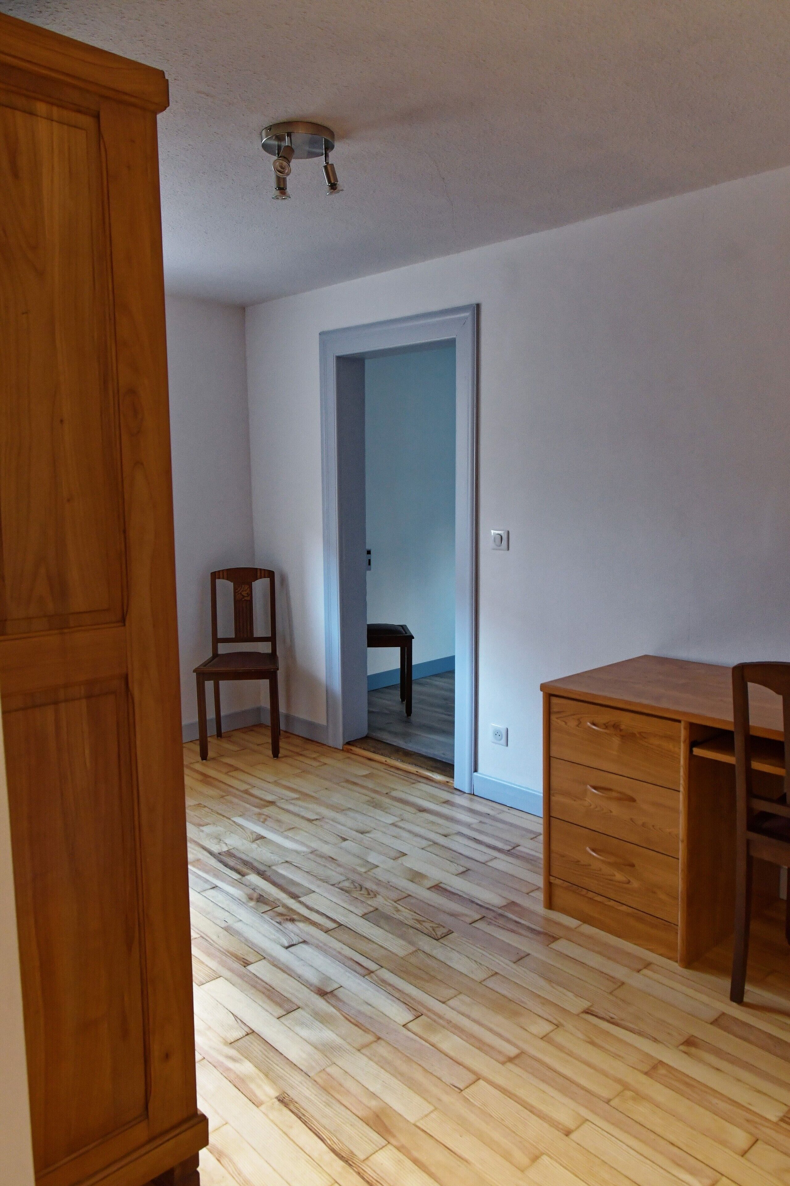 Una habitación con piso de madera, un escritorio, una silla y un armario.