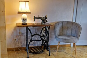 A vintage sewing machine on a wooden table with a lamp, a grey upholstered chair, and a wooden floor. - Holiday Home "Chez Jeanne, Charming House" with Private Garden and Wi-Fi (Dossenheim-sur-Zinsel)