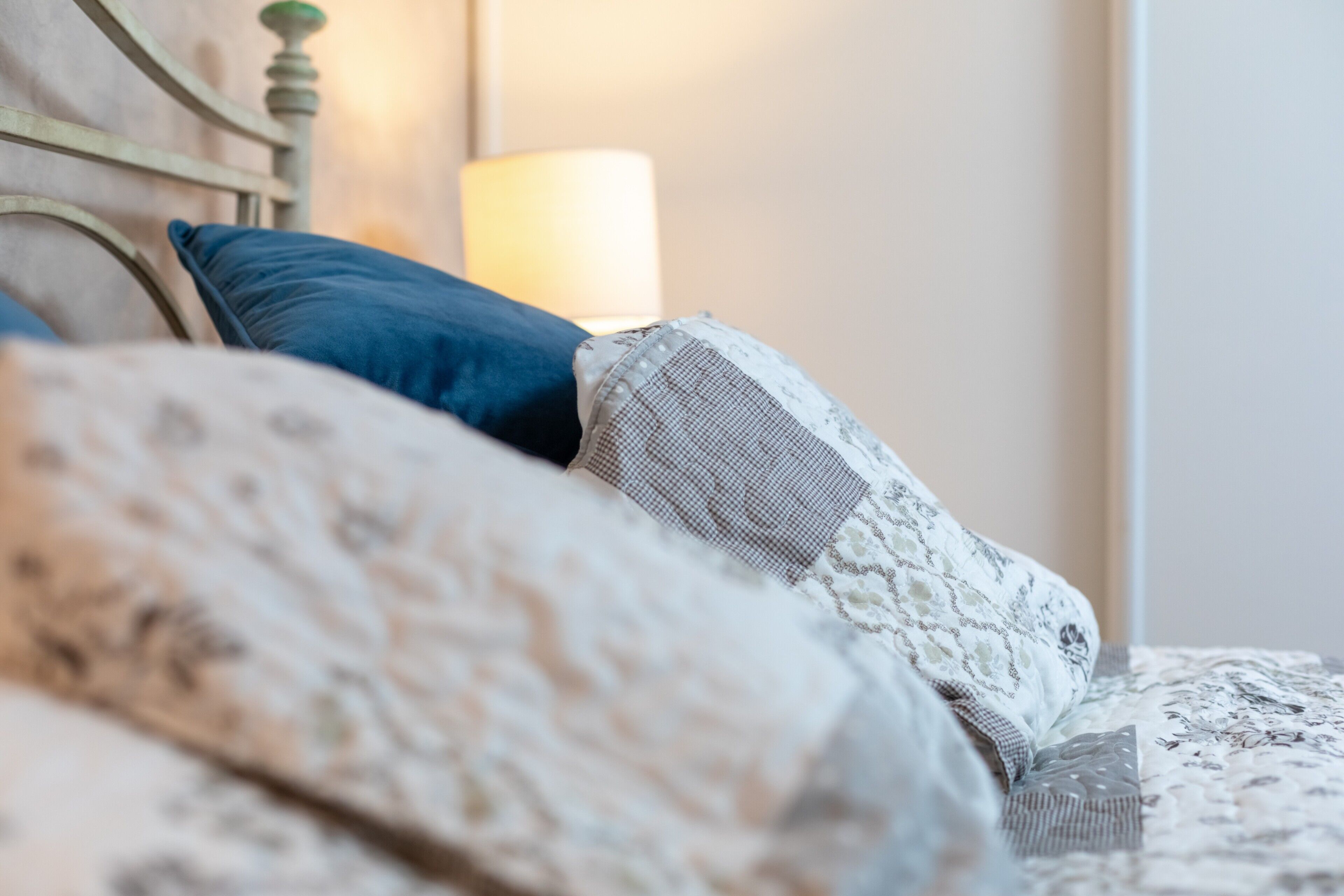 Un lit avec une literie et des oreillers à motifs, une tête de lit et une lampe de chevet.