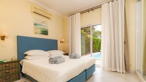 A bedroom with a large bed, a nightstand, a painting, and a view of a swimming pool. - Villa "Mng Elliott 50" with Private Pool and Wi-Fi (Vale do Lobo)