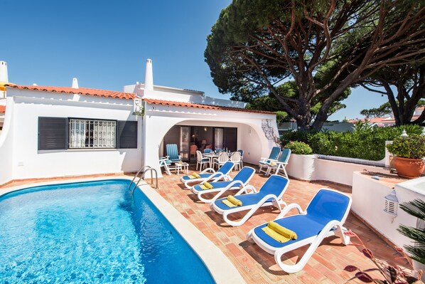 A poolside area with lounge chairs, a pool, and a building with a tiled roof.