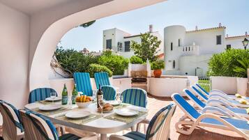 An outdoor dining area with a table set for two, blue-striped chairs, and a grill.