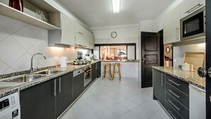 Une cuisine moderne dotée de plans de travail en granit, d’appareils électroménagers en acier inoxydable et d’un îlot central avec des tabourets.
