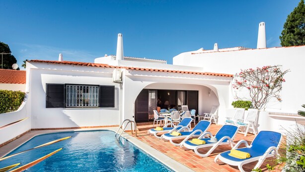 Une piscine avec des chaises longues, un patio couvert et un bâtiment blanc doté d’un toit en tuiles.