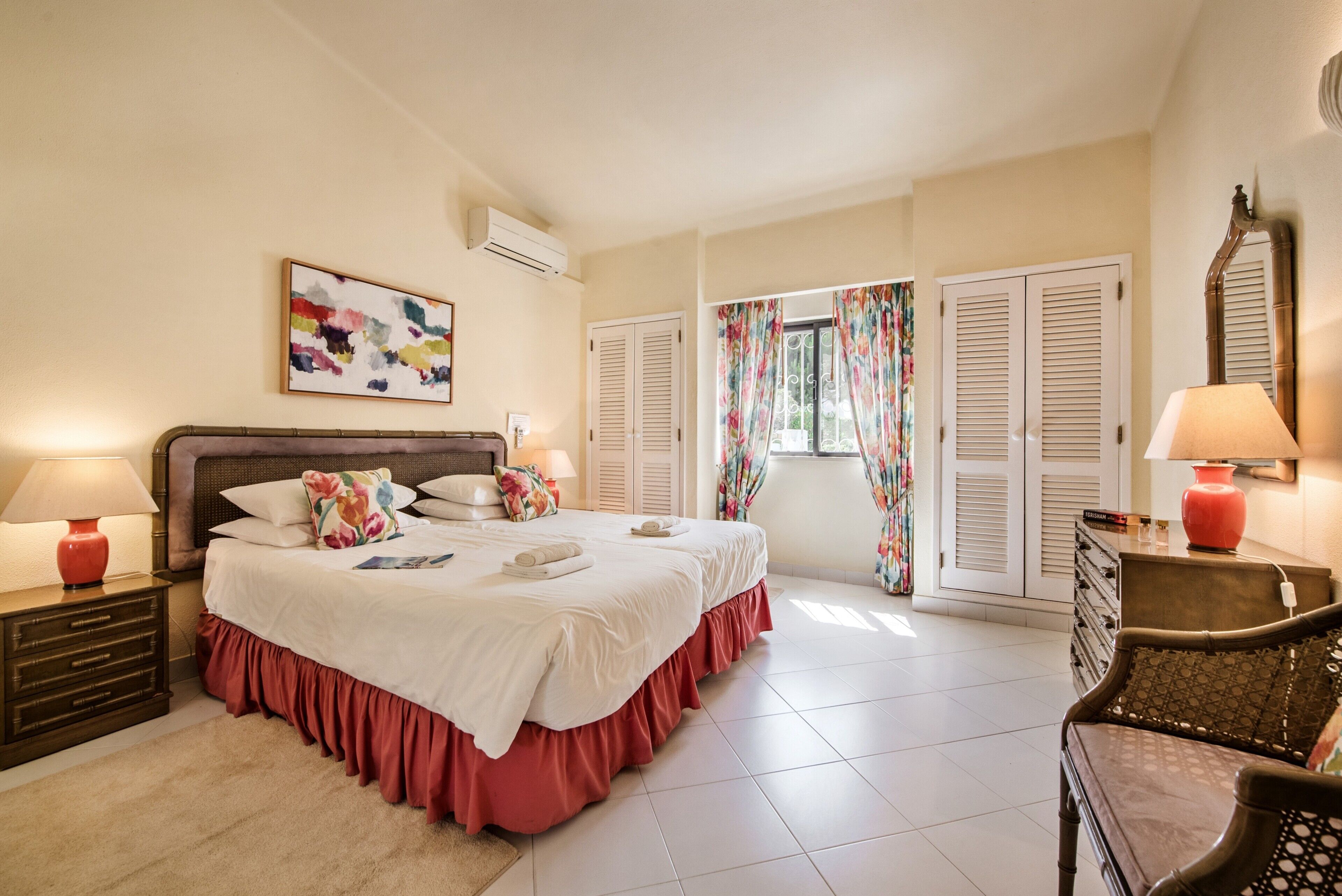 Une chambre à coucher comprenant un lit, deux tables de chevet avec des lampes, une commode, une chaise et une fenêtre avec des rideaux.
