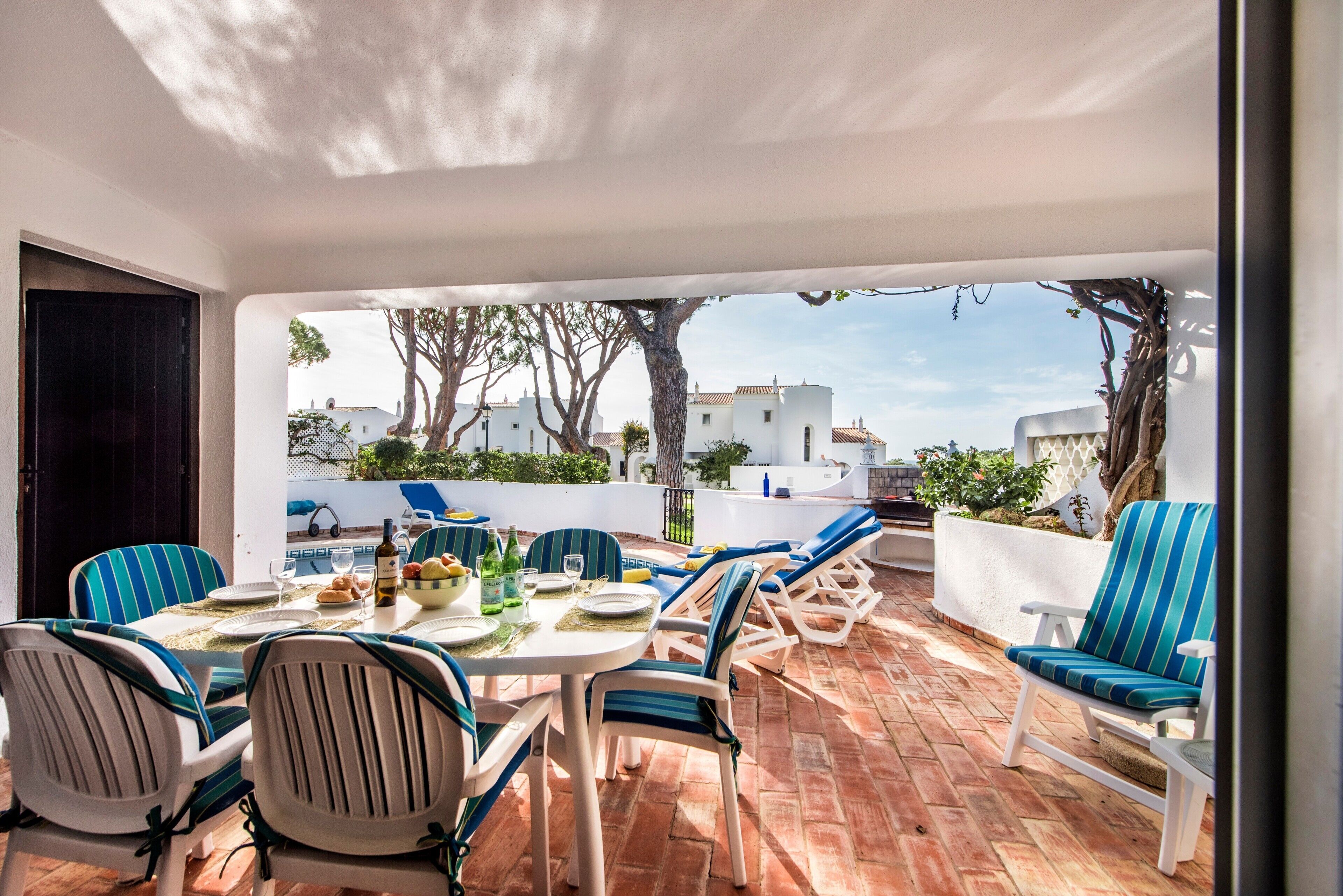 Une terrasse extérieure avec une table dressée pour le repas, entourée de chaises à rayures, et une vue sur des bâtiments en arrière-plan.