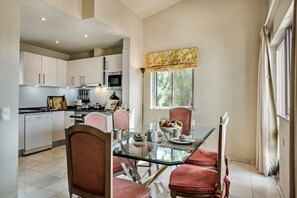 Una cocina moderna con armarios blancos, una mesa de comedor de vidrio y sillas rojas.