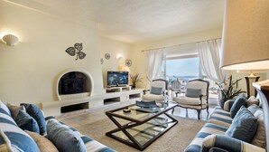 Un salon comprenant un canapé, des fauteuils, une table basse, une cheminée, un téléviseur et une vue sur l’extérieur.