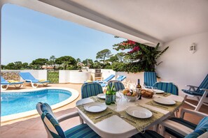 Un espace repas avec vue sur la piscine, des sièges d’extérieur et une table dressée pour deux personnes.