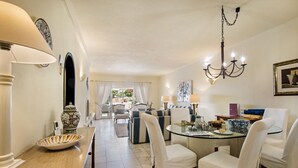 Un coin repas avec une table en verre, des chaises à revêtement blanc, un lustre et un vase posé sur la table.