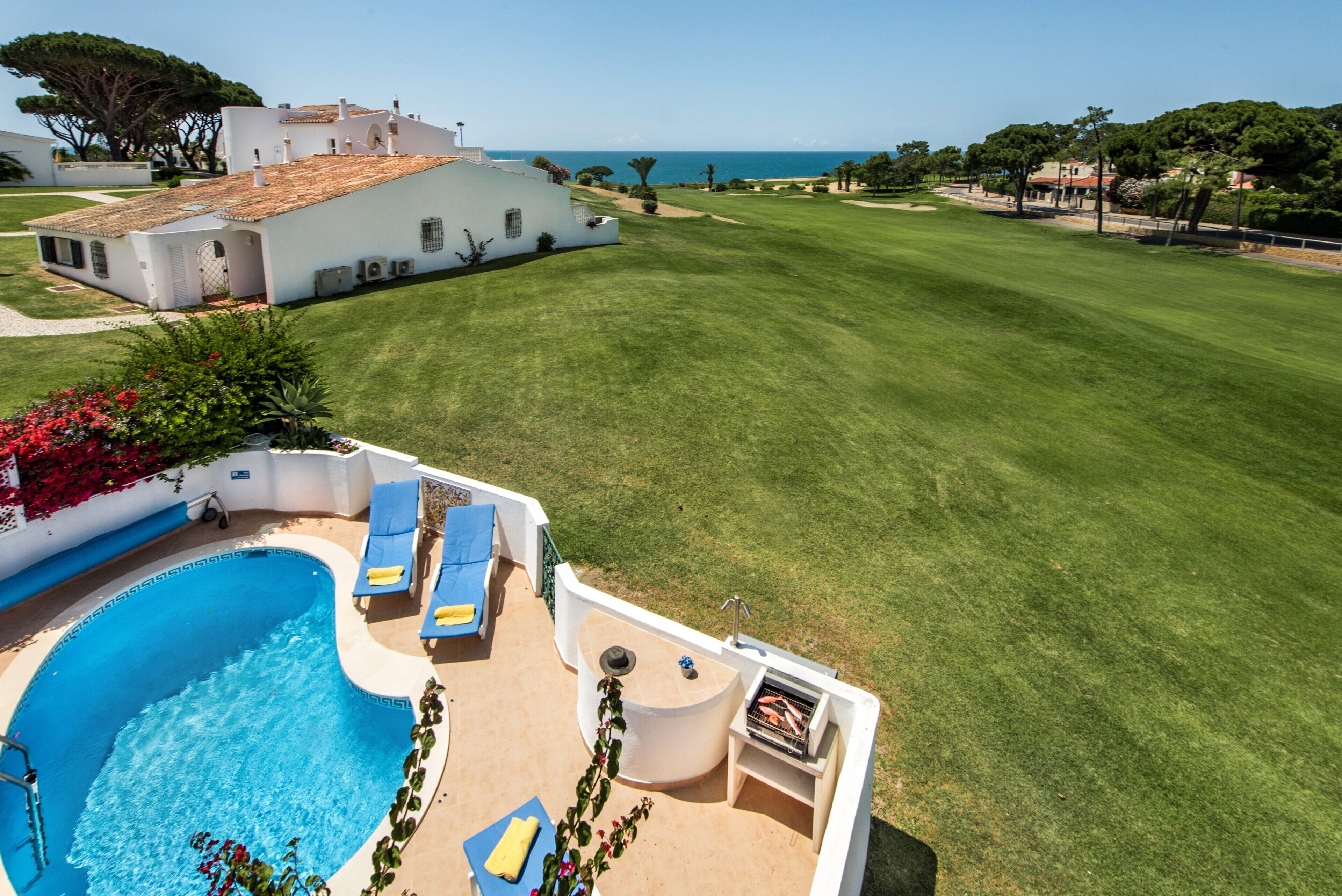 A pool with lounge chairs, a barbecue area, and a view of the sea.