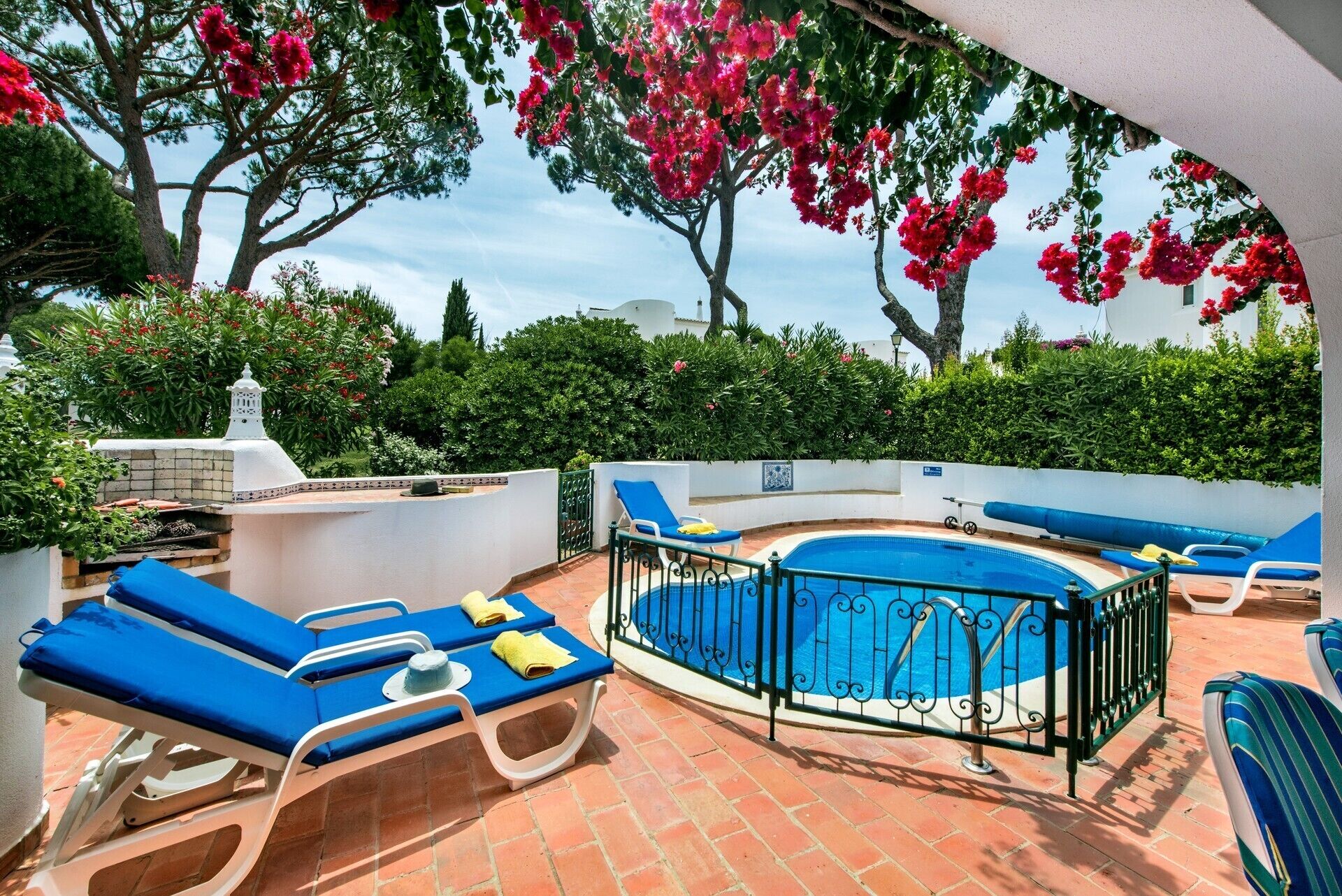 A pool area with blue lounge chairs, a small pool, and a white wall with a chimney.