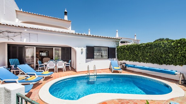 Piscina com espreguiçadeiras, mesa e área coberta.