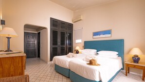 Quarto com cama, mesas de cabeceira, abajur, guarda-roupa e porta que dá para outro espaço.