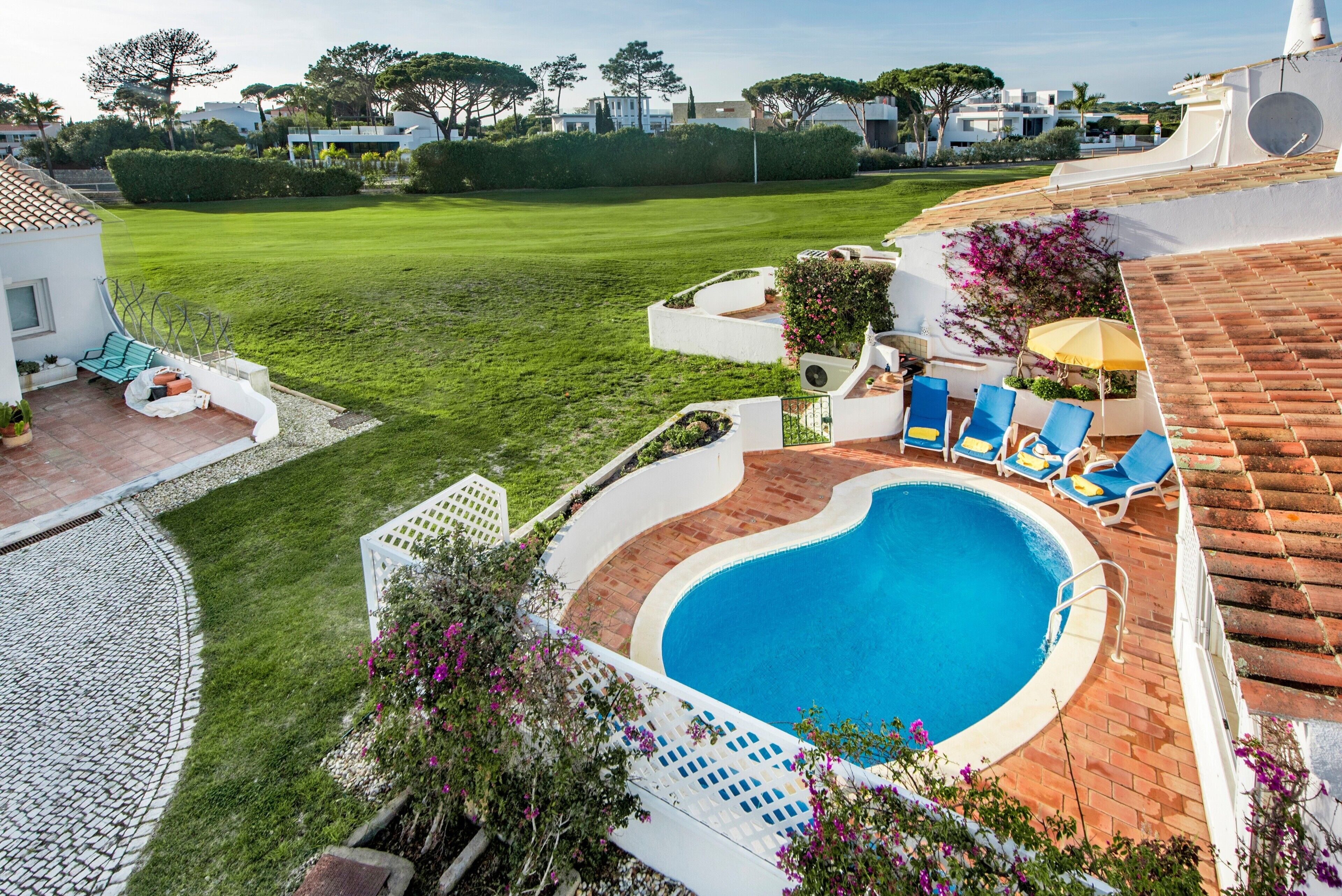 Ein Swimmingpool mit Liegestühlen, eine Terrasse und ein gepflegter Rasen.