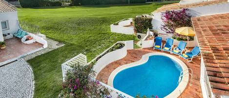 Una piscina con sillas de descanso, un área de patio y un césped bien cuidado.