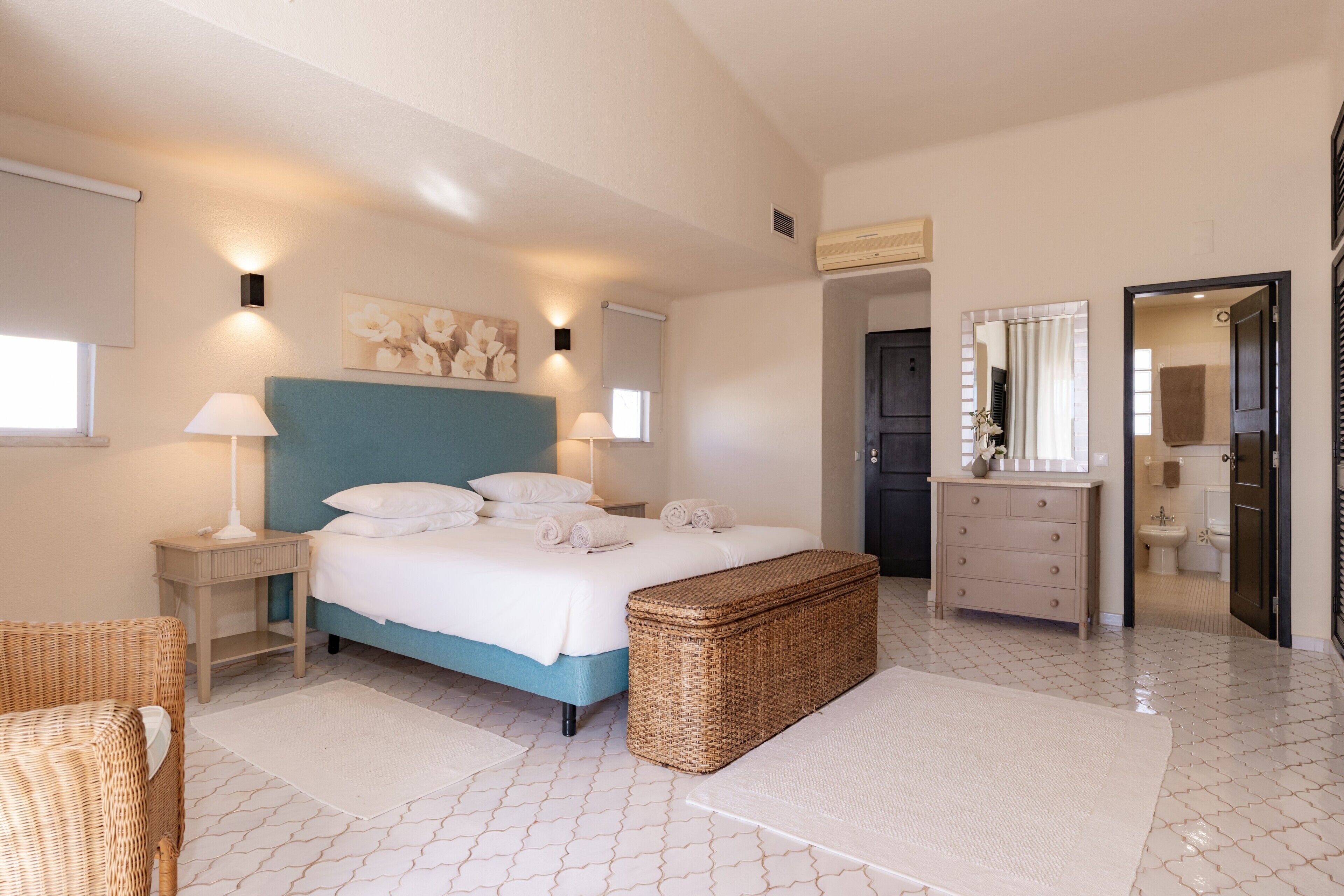 Een slaapkamer met een bed, nachtkastjes, een kaptafel en een zichtbare badkamer door een open deur.