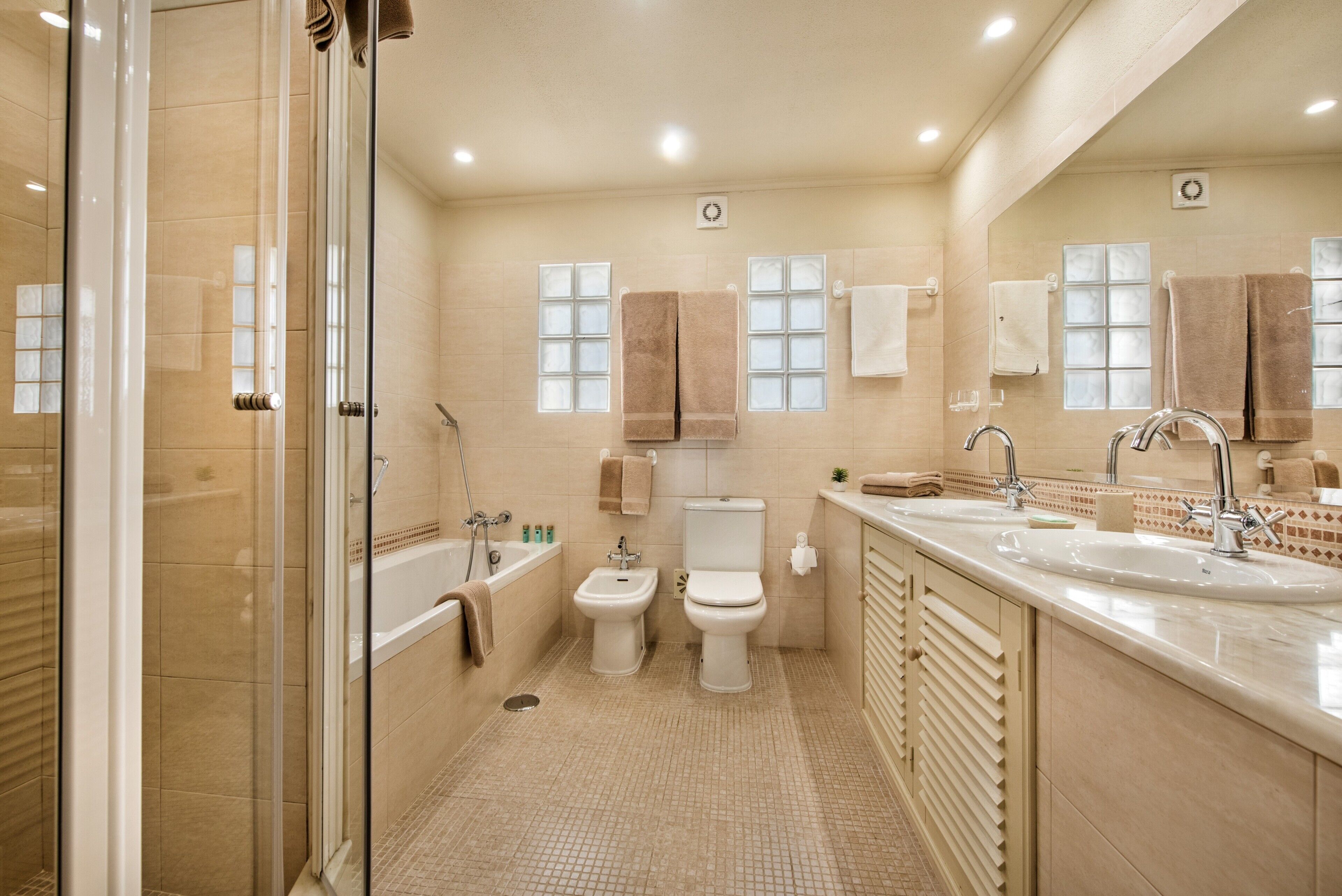 A modern bathroom with a glass shower enclosure, a bathtub, a toilet, and a large vanity with a sink.