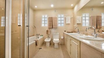 A modern bathroom with a glass shower enclosure, a bathtub, a toilet, and a large vanity with a sink.